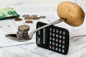 A spoon on a calculator with a pile of coins on one end and a potato on the other symbolizing weighing the pros and cons of cost of living in Miami Gardens Florida.