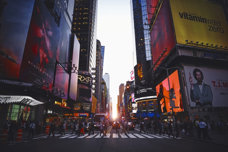 people walking across the street with Time Square lights in the background.