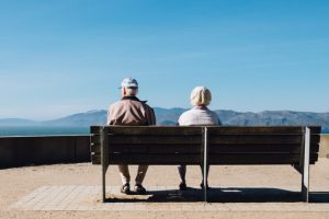 Two seniors sitting on a bench somewhere near the seaside, enjoying their travel time before settling down in one of Longmont neighborhoods for seniors.