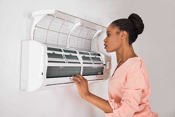 Young African Woman Checking Air Conditioner that isn't blowing cold air